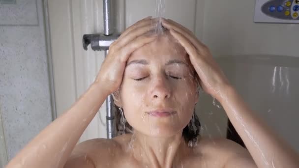 Nær en vakker kvinne vasker hun sitt lange, mørke hår i dusjen, tar seg i akt, keratinmaske, skyller sjampo og balsam, sterkt hår, vasker seg – stockvideo