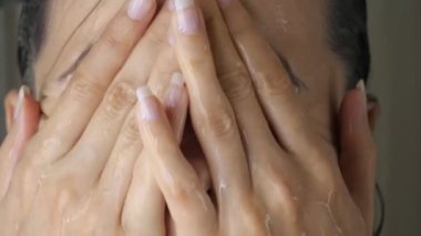 Duş banyosundaki yüzü su damlalarıyla dolu genç bir kadının portresini yakından çek. Kız ellerini yüzüne doğru uzatır, nefes alır, gözlerini açar.
