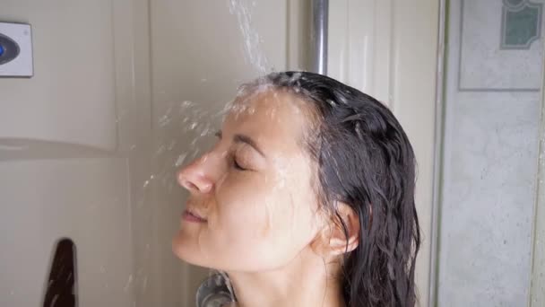 Młoda kobieta bierze prysznic stojąc pod strumieniem wody. Dziewczyna zmywa szampon z włosów stojąc pod ciepłym strumieniem prysznica — Wideo stockowe