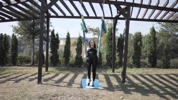 Молодая женщина висит вверх ногами. Акробатика и антигравитационная йога в природе — стоковое видео