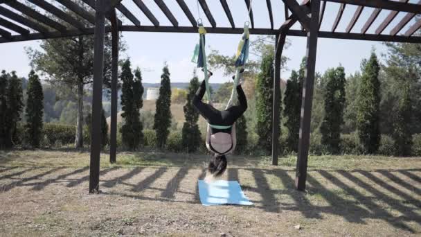 Jonge vrouw die luchtyoga beoefent in het park. Dit type yoga op speciale stoffen doeken. De man die yoga beoefent vliegt in hangmatten. Super slow motion — Stockvideo