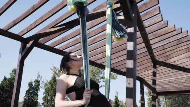 Молода жінка практикує антигравітаційну йогу на гамаку в парку. Дівчинка займається мухами, літом з аерозйоги в природі. — стокове відео