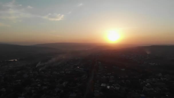Aerial fly over village at sunrise or sunset. Aerial camera bird eye view. Unsurpassed view of sun which illuminates whole landscape. Thick fog covered all fields — Stock Video
