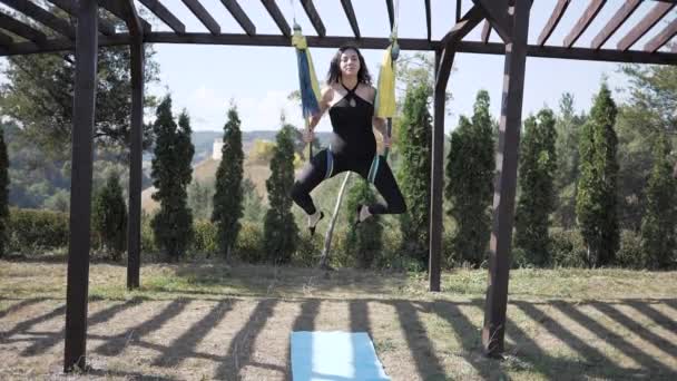 若い女性は公園でハンモックで反重力、空中ヨガを練習します。女の子はフライヨガに従事している。夏になると — ストック動画