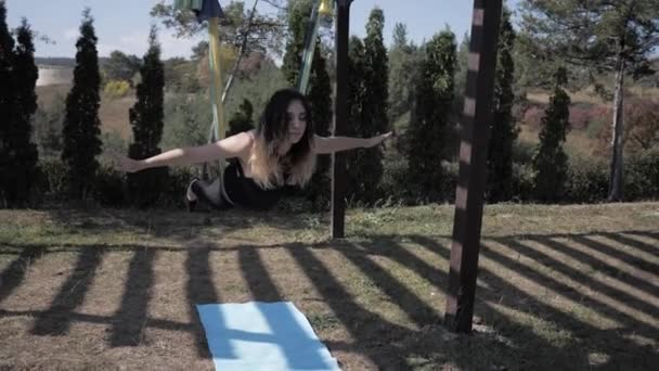 Jonge sportvrouw doet vliegyoga in Park. Meisje doet anti-zwaartekracht, luchtyoga op hangmat bij zonsondergang. Buiten. Langzame beweging — Stockvideo