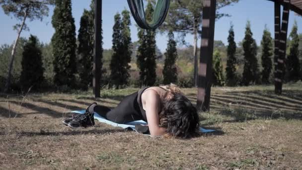 Гибкая женщина, занимающаяся йогой в парке, делает сложные упражнения для разминки. Медленное движение — стоковое видео