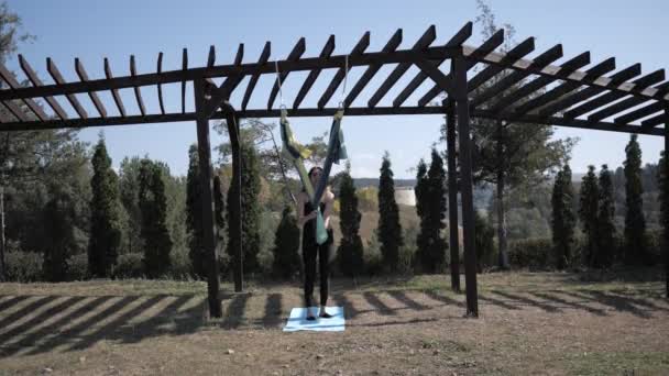 Mooie jonge vrouw doet anti-zwaartekracht vliegen yoga in hangmatten buiten. Uitbreidingsoefeningen in fitnesstraining in het park. Langzame beweging — Stockvideo