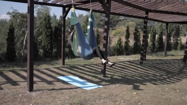 Jonge vrouw beoefent anti-zwaartekracht yoga op hangmat in Park. Meisje is bezig met vliegen, luchtyoga zomer in de natuur — Stockvideo