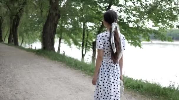 긴 머리를 가진 젊은 여자의 모습이 공원의 호수를 따라 걸어 다닌다. 뒤에서 본 모습 — 비디오