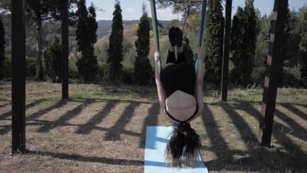 Jeune femme pratiquant le yoga aérien dans le parc. Ce type de yoga sur des toiles de tissu spécial. Homme pratiquant le yoga voler dans les hamacs. Super ralenti — Video