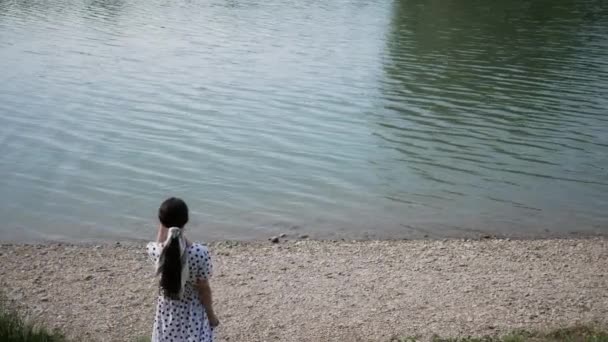 Молодая женщина спускается к берегу озера или моря и ищет кого-то с глазами вдоль горизонта — стоковое видео