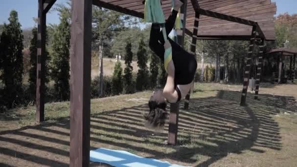 Ung kvinna som utövar flygyoga flyger i hängmattor i parken. slow motion — Stockvideo