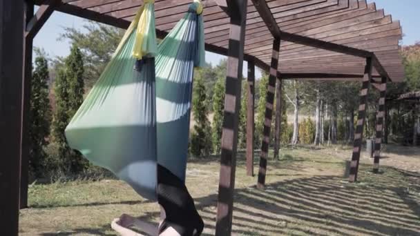 Młoda wysportowana kobieta robi zestaw ćwiczeń asana w powietrzu jogi na hamaku w Park. Latająca joga — Wideo stockowe