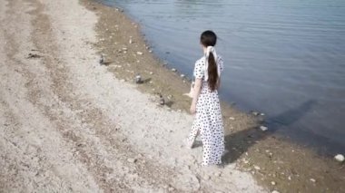 Uzun elbiseli, genç ve romantik bir kadın rüzgârda çırpınıyor körfez kıyısında yürüyor.