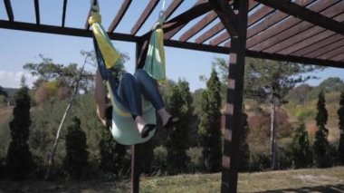 Genç bayan sporcu parktaki hamakta anti-yerçekimi yoga egzersizleri yapıyor.