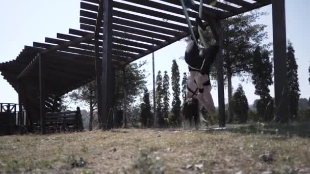 Молодая спортсменка тренируется в парке, выполняя трюки вверх ногами на гамаке — стоковое видео