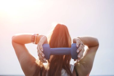 Dambıllarla egzersiz yapan genç bir kadın. Arkadan bak. Sağlıklı yaşam tarzı kavramı