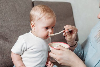 Genç anne kızını bir kaşık meyve püresiyle besliyor.
