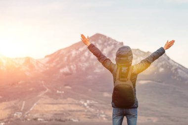 Dağların tepesinde kollarını havaya kaldırmış bir yürüyüşçü. Arkadan görünüm