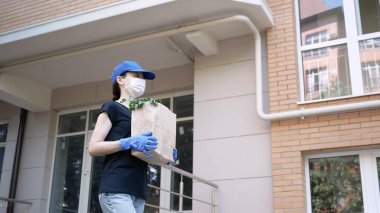 Kurye, koruyucu maskeli kurye ve tıbbi eldivenli teslimatçı paket yemek getiriyor. Karantina altında teslimat hizmeti, hastalık salgını, koronavirüs covid-19 salgını. Evde kal..