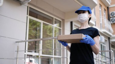 Kurye, koruyucu maskeli kurye ve tıbbi eldivenli adam küçük bir paket teslim ediyor. Karantina altında teslimat hizmeti, hastalık salgını, koronavirüs covid-19 salgını. Evde kal..