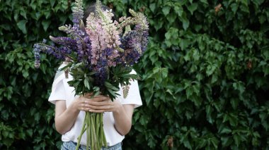 Tanımlanamayan bir kadının, yeşil duvarın arka planında elinde bir buket çiçek tutması..
