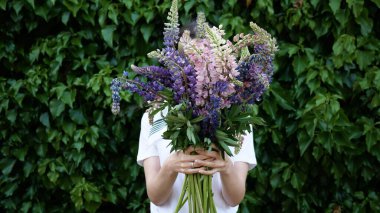 Güzel bir buket çiçek, elinde onu yeşil bitki duvarının arkasında elinde tutan tanınmayan genç bir kadının ellerinde..