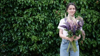 Yeşil bir çalı duvarının yanında elinde bir buket çiçekle gülümseyen esmer kadın. Boşluğu kopyala.