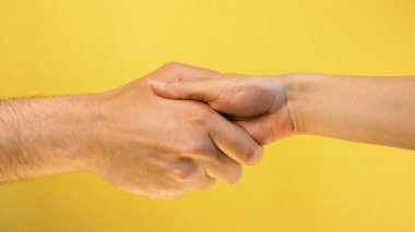 Sarı arka planda çıplak kadın ve erkeğin el sıkışması izole edildi. Kadın ve erkek elleri selamlıyor.