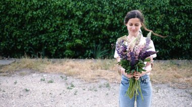 Genç kadın çiçeklere bakıyor, onları kokluyor ve gülümsüyor. Romantik bir kadın ve bir buket çiçek. Boşluğu kopyala.