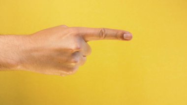 Erkek eli sarı arka planda izole edilmiş bir şeyi ya da birini işaret ediyor. Yakın çekim.