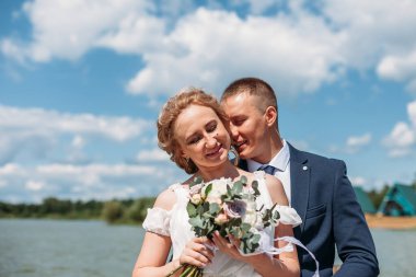 Beyaz elbiseli genç çift ve mavi elbiseli damat gölün ortasında poz veriyor ve sarılıyorlar. Yaz mevsiminde doğada kavramsal düğün. Düğün, aile, aşk hikayesi konsepti.