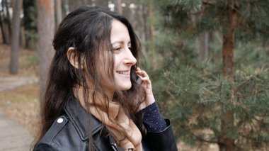 Halk parkında yürürken gülümseyen ve telefonda konuşan bir kadın. Arayan kişiyi duyduğuna sevindi..