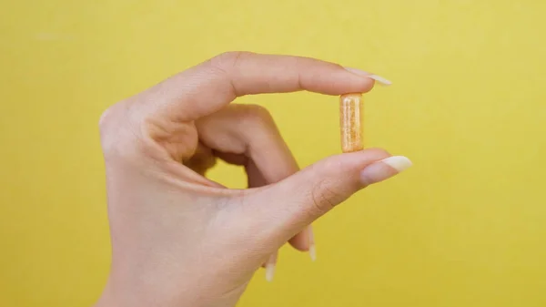 Kadın Eli Parmaklarını Sarı Arka Planda Izole Edilmiş Kapsül Hapıyla — Stok fotoğraf