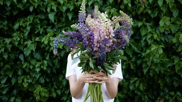 Güzel bir buket çiçek, elinde onu yeşil bitki duvarının arkasında elinde tutan tanınmayan genç bir kadının ellerinde..