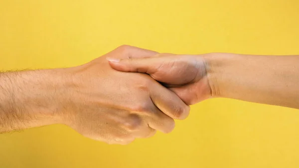 Closeup of hand shake of nude man and woman on yellow background isolated. Woman and man hands greeting.