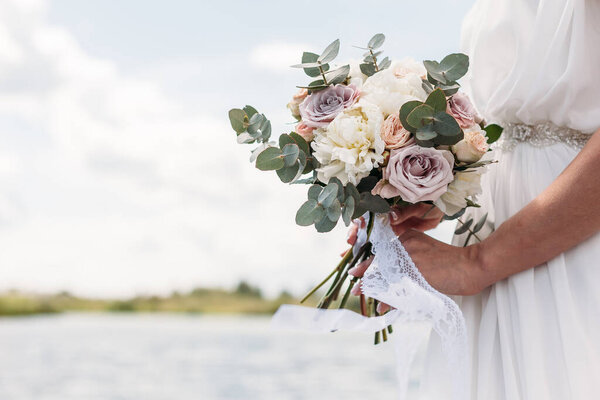 Bridal bouquet. Beautiful wedding pink and white flowers in hands of the bride. Close up outdoor shot against nature background. Wedding bouquet in bride's hands. Copy space