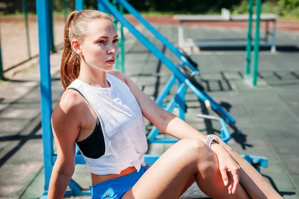 Sporcu genç sarışın kadın spor sahasında antrenmanlardan sonra dinleniyor..