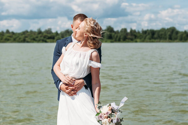 Groom hugs bride tender from behind while they enjoy the wind over the lake 