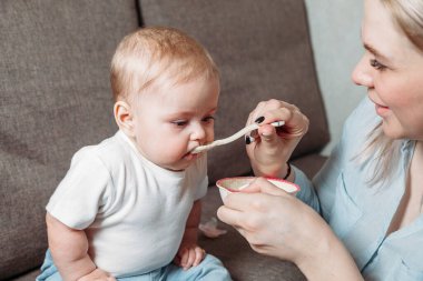 Genç anne kızını bir kaşık meyve püresiyle besliyor.