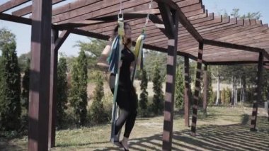 Genç atletik kadın hamakta yoga yapıyor. Asana - Hatha yogası yaparken takınılan duruş. Park