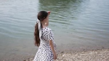 Genç bir kadın gölün kıyısına geldi ve gözleri ile birini arıyor ve parmağını oraya doğrultuyor.