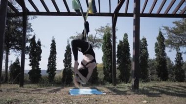 Genç atletik kadın hamakta yoga yapıyor. Asana - Hatha yogası yaparken takınılan duruş. Park