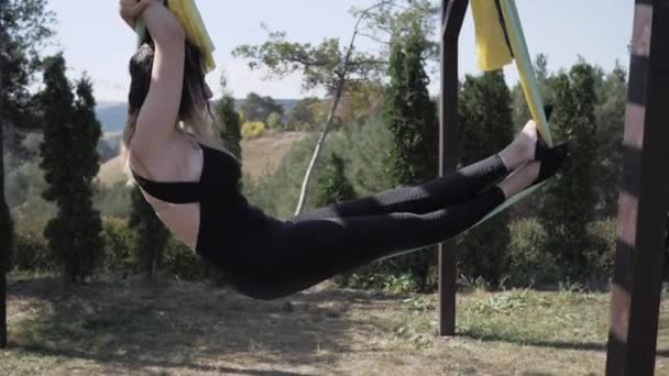 Jovem atleta feminina realiza exercícios de ioga aero na rede ao ar livre no parque — Vídeo de Stock