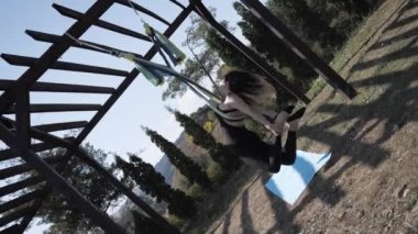 Genç bayan sporcu, parktaki hamakta aero yoga egzersizleri yapıyor. dairesel kamera döndürmesi