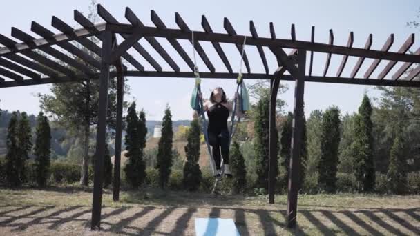 Athlétique jeune femme faisant du yoga aérien sur hamac dans le parc dans la nature, faire des exercices acrobatiques complexes — Video