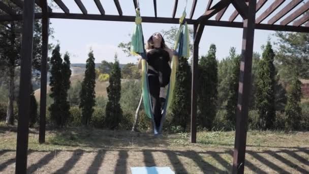 Jonge atletische vrouw doet luchtyoga op hangmat. Asana - houding aangenomen in het uitvoeren van hatha yoga. Park — Stockvideo