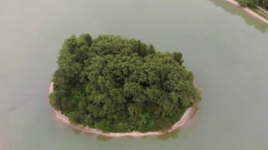 Geniş gölün ortasındaki yeşil ağaçlı güzel dairesel adanın havadan aşağı 4k görüntüsü.