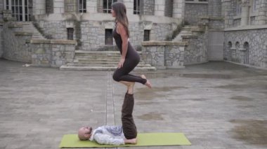 Turp gibi bir çift, eşiyle açık havada akro yoga yapıyor. Akrobatik egzersiz yapan bir çift. Dişi akrobat erkek ortağının bacaklarında dengede duruyor. Namaste