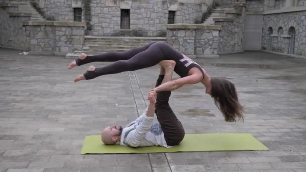 Ajuste pareja deportiva practicando acro yoga con pareja juntos en la esterilla al aire libre. Pareja haciendo ejercicio acrobático. Acróbata hembra se equilibra en las piernas de su pareja masculina — Vídeos de Stock